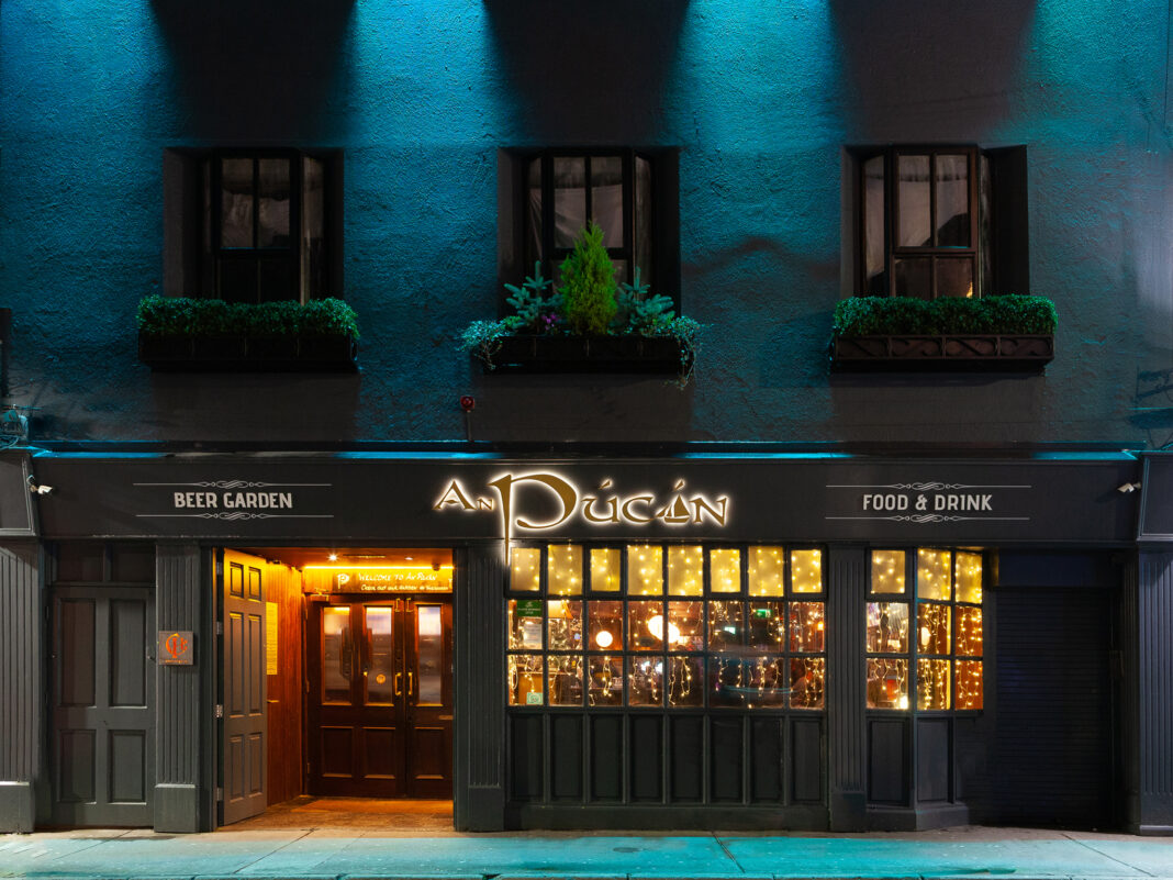 Illuminated facade of An Púcán pub on Forster Street in Galway at night