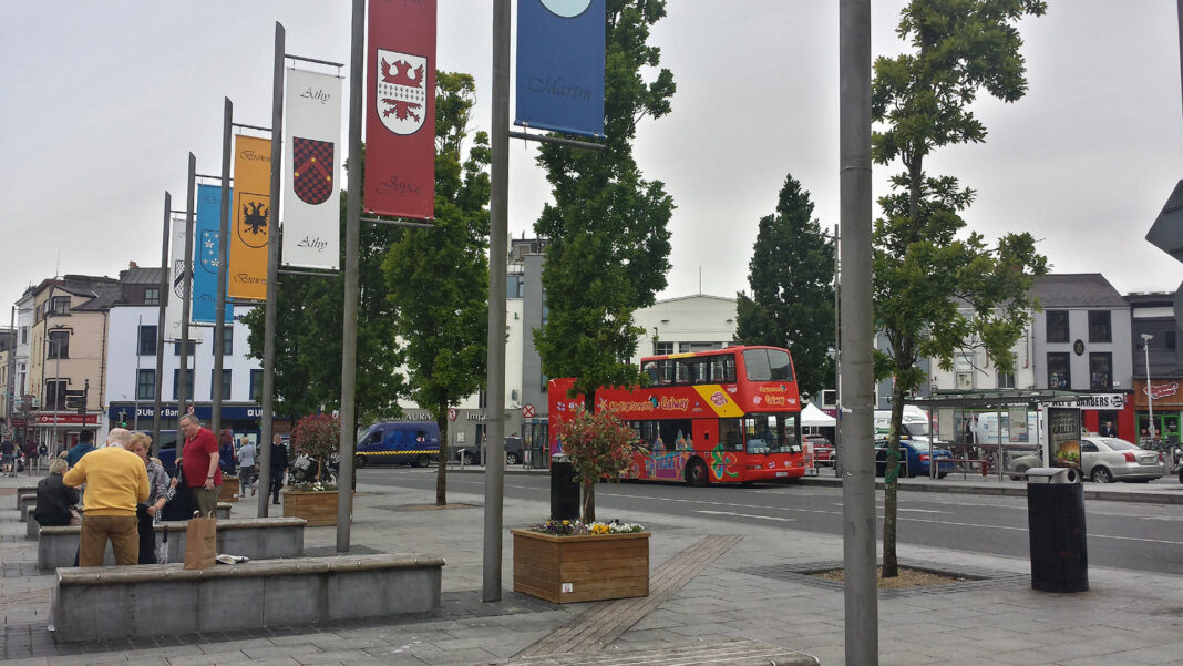 Galway Hop-On Hop-Off Bus: Is the City Sightseeing Tour Worth It? Red open-top Galway City Sightseeing bus beside the tribal flags at Eyre Square