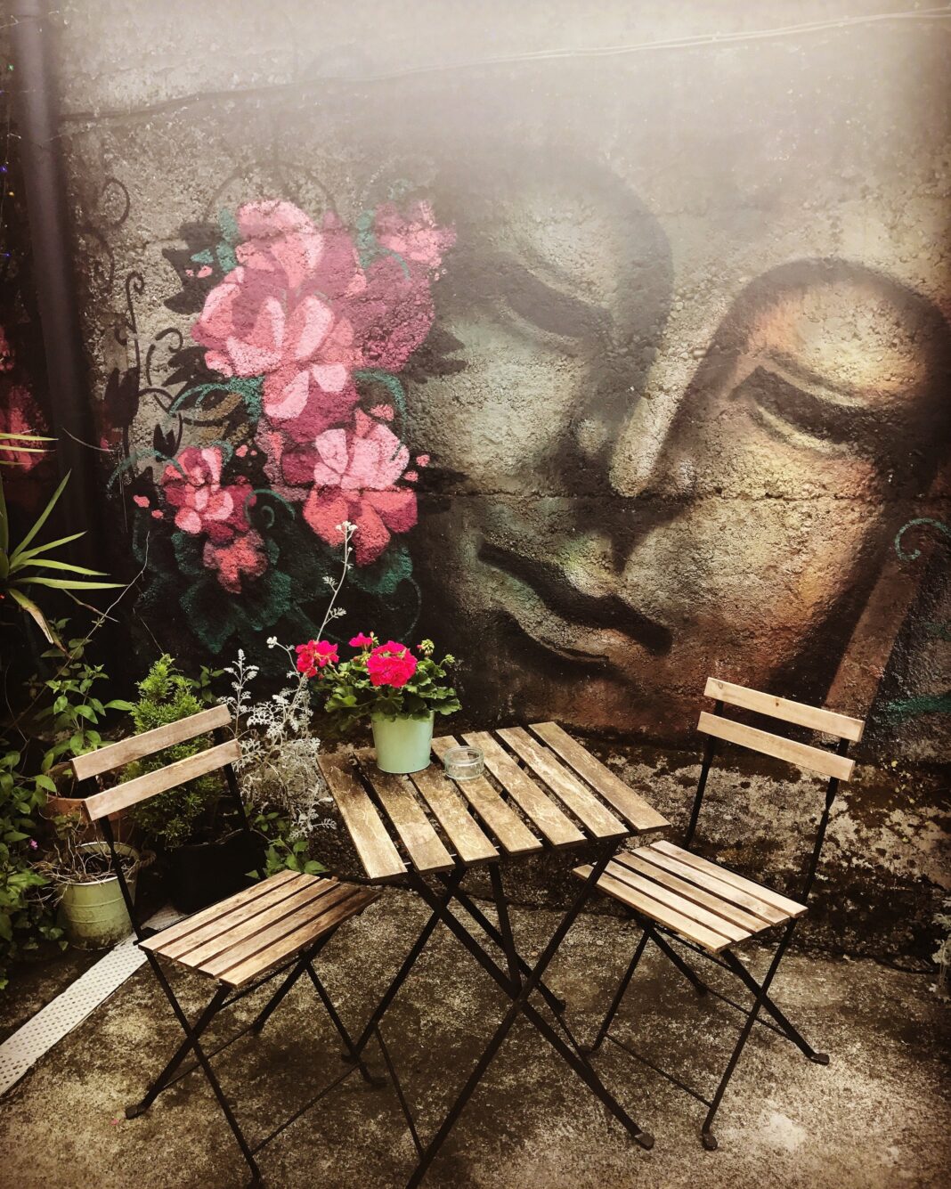 The Secret Garden Galway: Tea, Treats and a West End Pause Wooden garden table and chairs beside flowers and a mural at The Secret Garden Galway