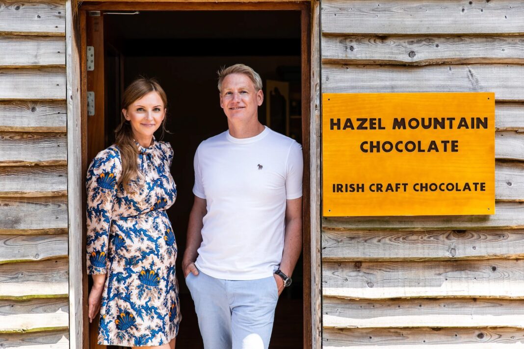 Two people at the timber workshop entrance beside the Hazel Mountain Chocolate sign