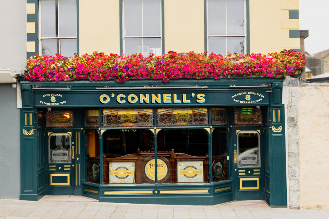 O’Connell’s Galway: An Old Front Bar and a Beer Garden Behind Eyre Square Green and gold facade of O’Connell’s Bar on Eyre Square with flower boxes above the entrance